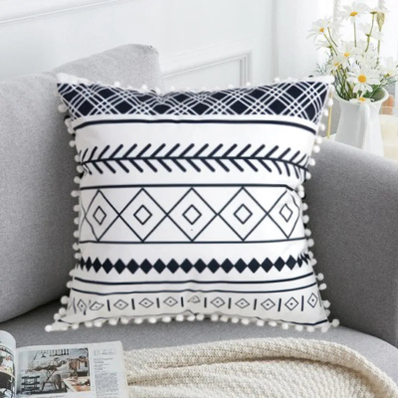 Multi-band black and white geometric throw pillow with navy accents and pom-pom edges