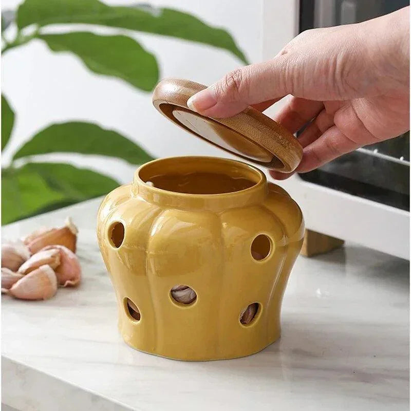 Hand lifting bamboo lid from mustard yellow vented ceramic garlic keeper jar