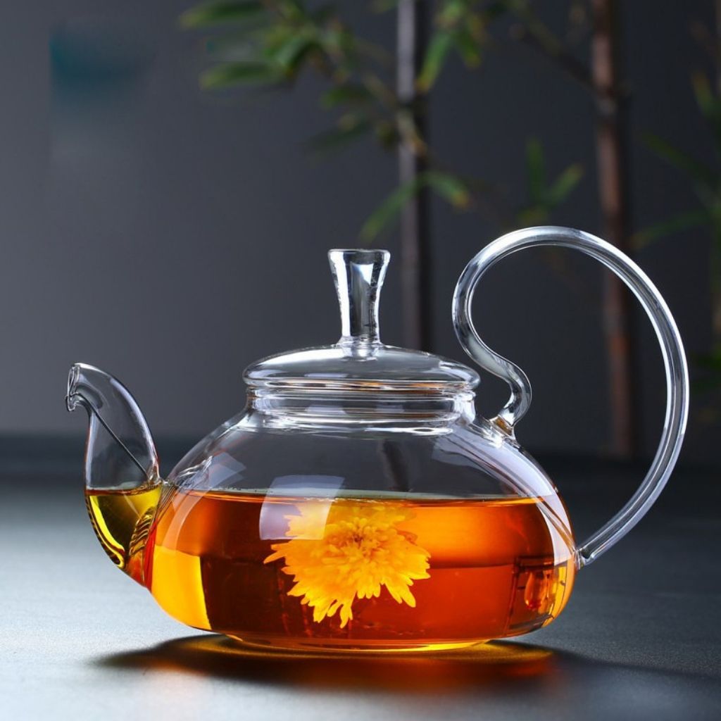 Blooming yellow chrysanthemum tea in clear glass teapot on dark reflective surface