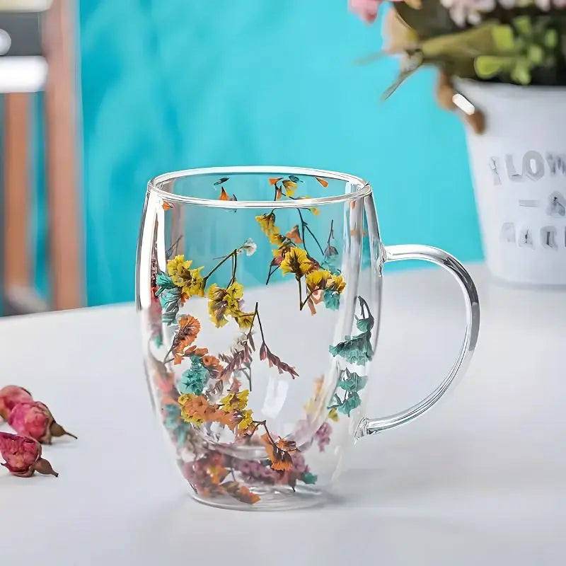 Double wall glass mug with suspended yellow and teal dried flowers on white surface