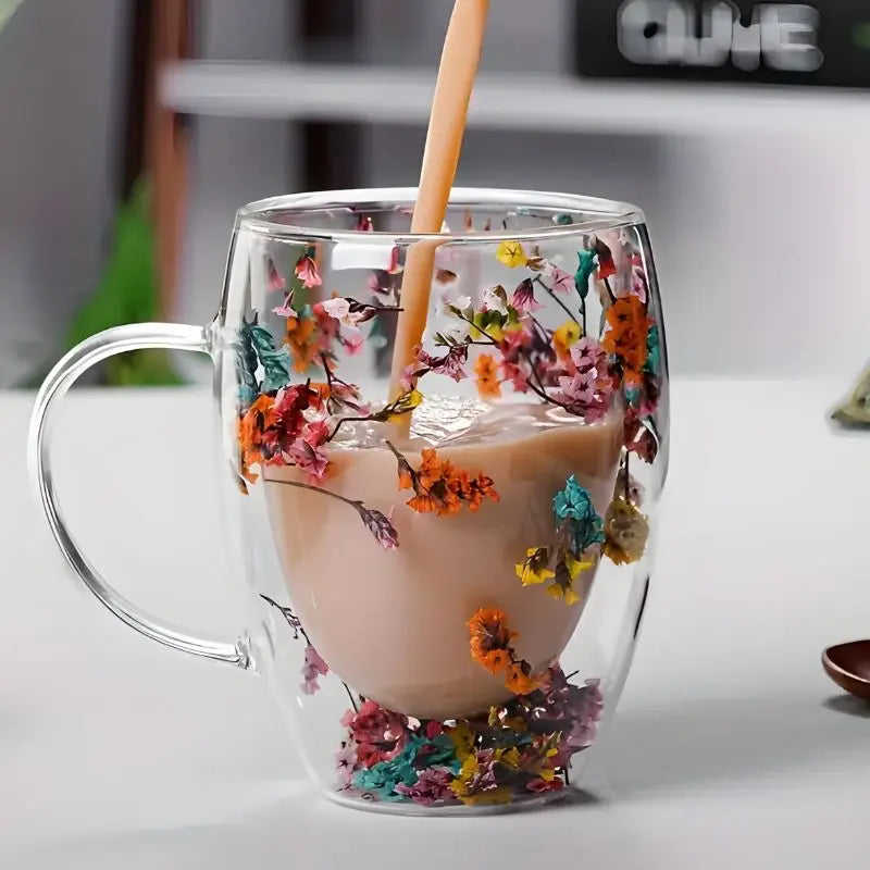 Pouring tea into double wall glass mug with wooden stirrer and suspended orange flowers
