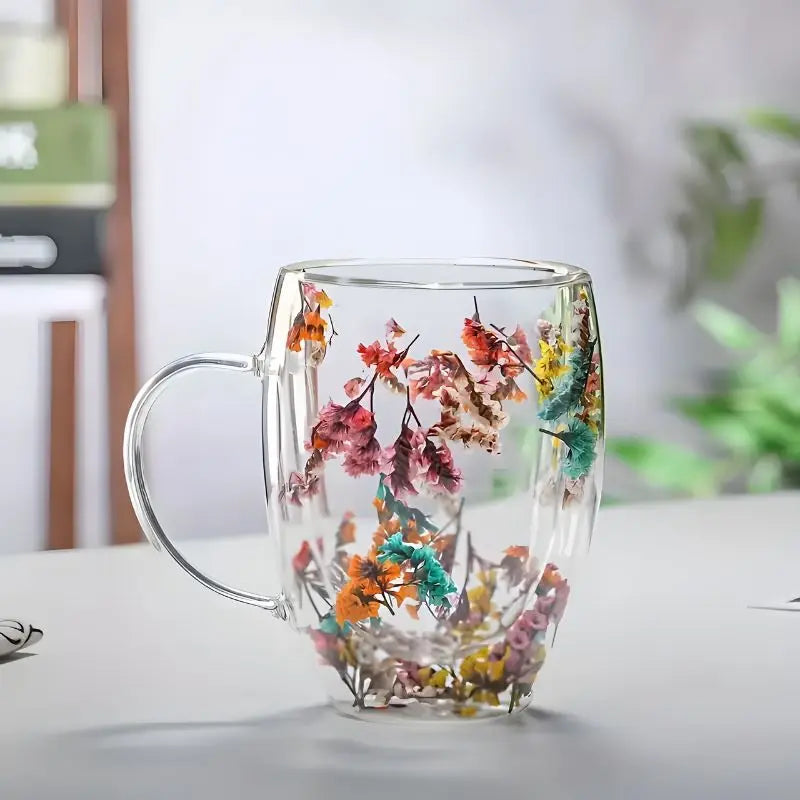 Boho dried flower glass mug with orange teal clusters on white tabletop