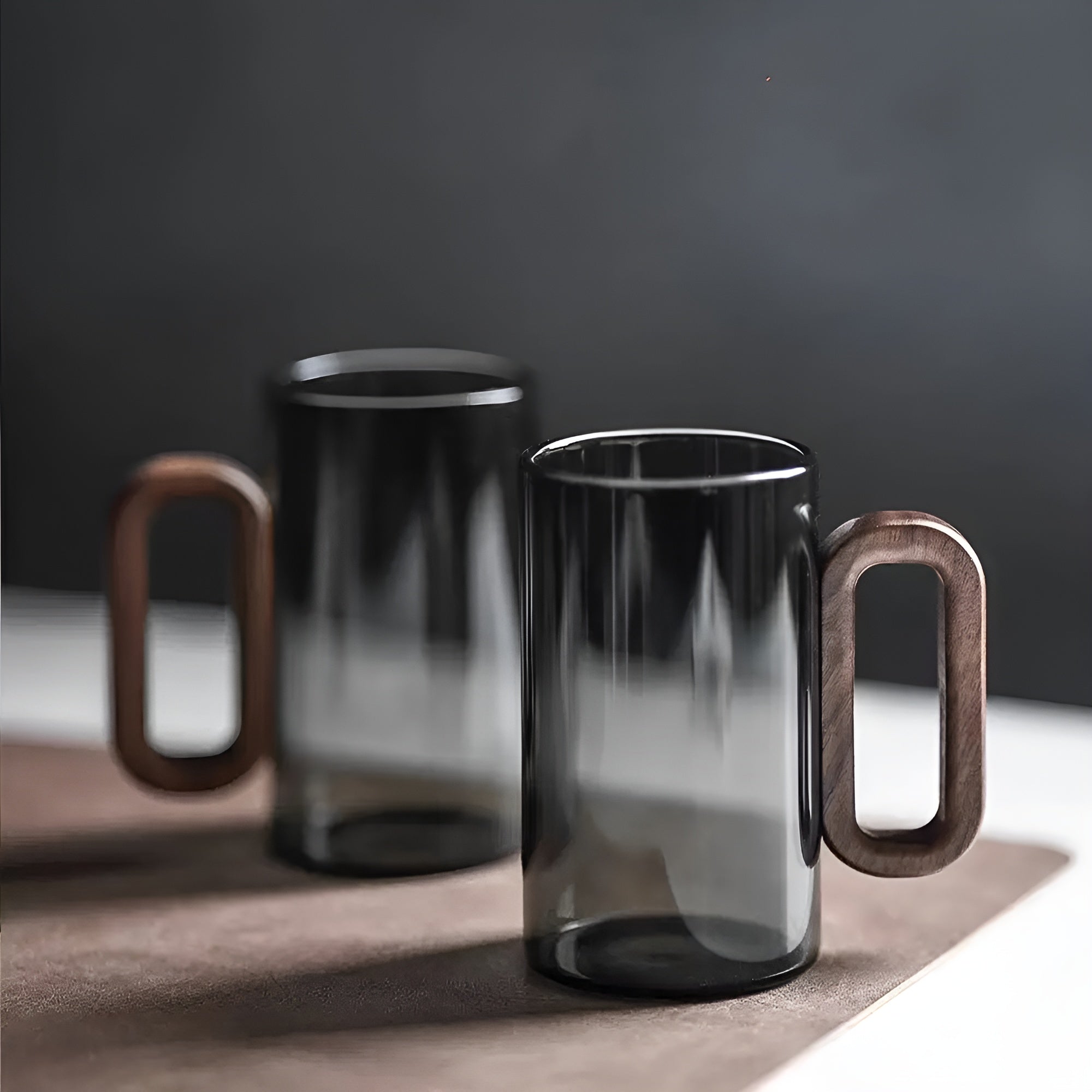 Pair of dark smoked glass mugs with wooden handles on light mat
