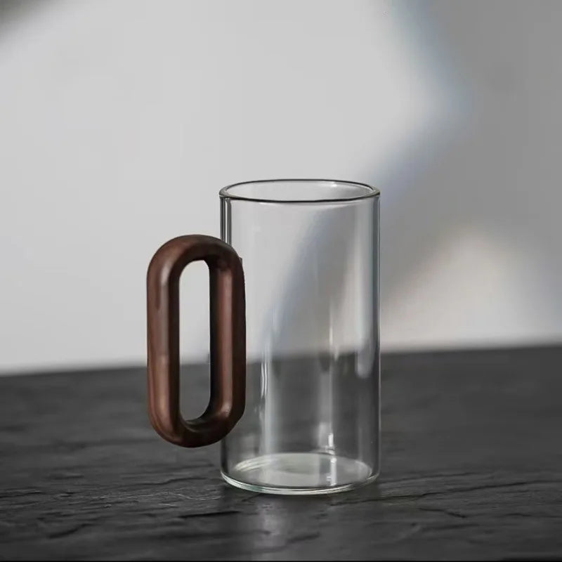 Clear glass highball mug with warm brown wooden handle on textured surface