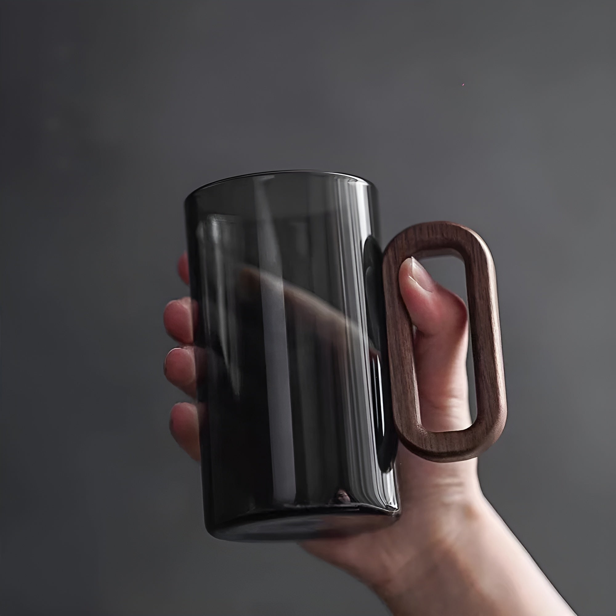 Hand holding single dark smoked glass mug with rectangular wooden handle