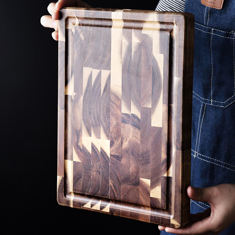 Vertical end grain acacia wood cutting board held by person in denim apron
