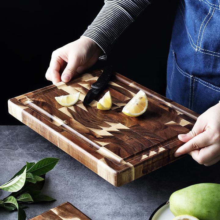 End grain acacia wood cutting board with juice groove holding lemons and knife