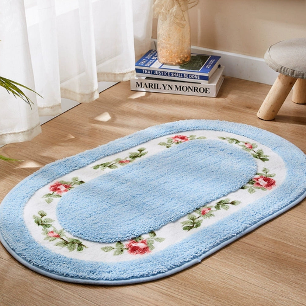 Light blue oval floral bath mat with non-slip backing on wood floor beside books