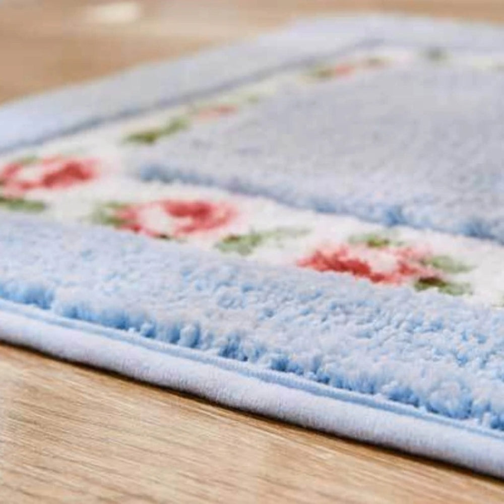Close-up of light blue oval bath mat with red rose floral border and plush microfiber texture
