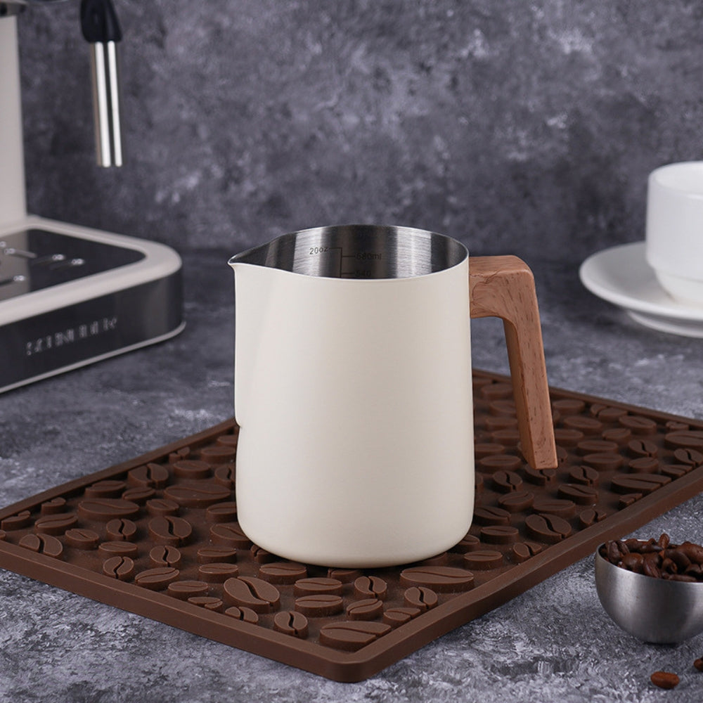 White matte coffee milk jug on coffee bean mat next to espresso machine for home brewing