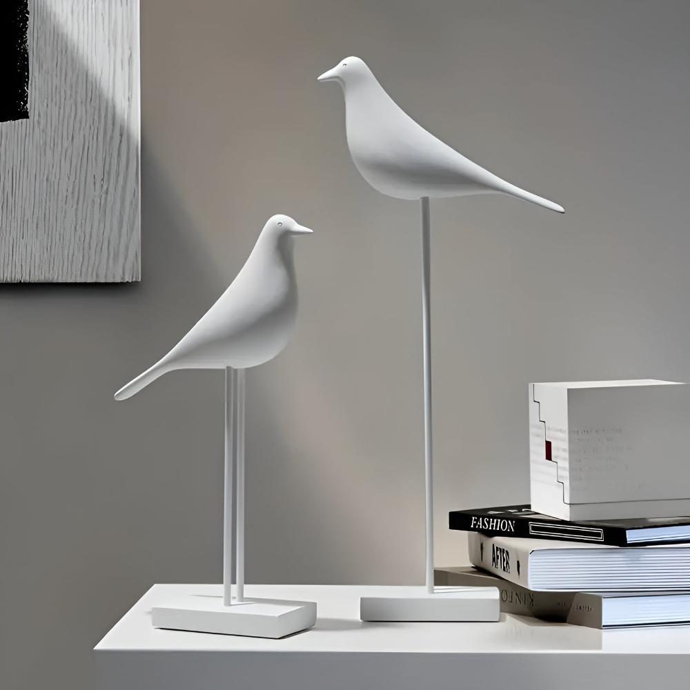 White abstract bird statues on slender stands beside books for home decor