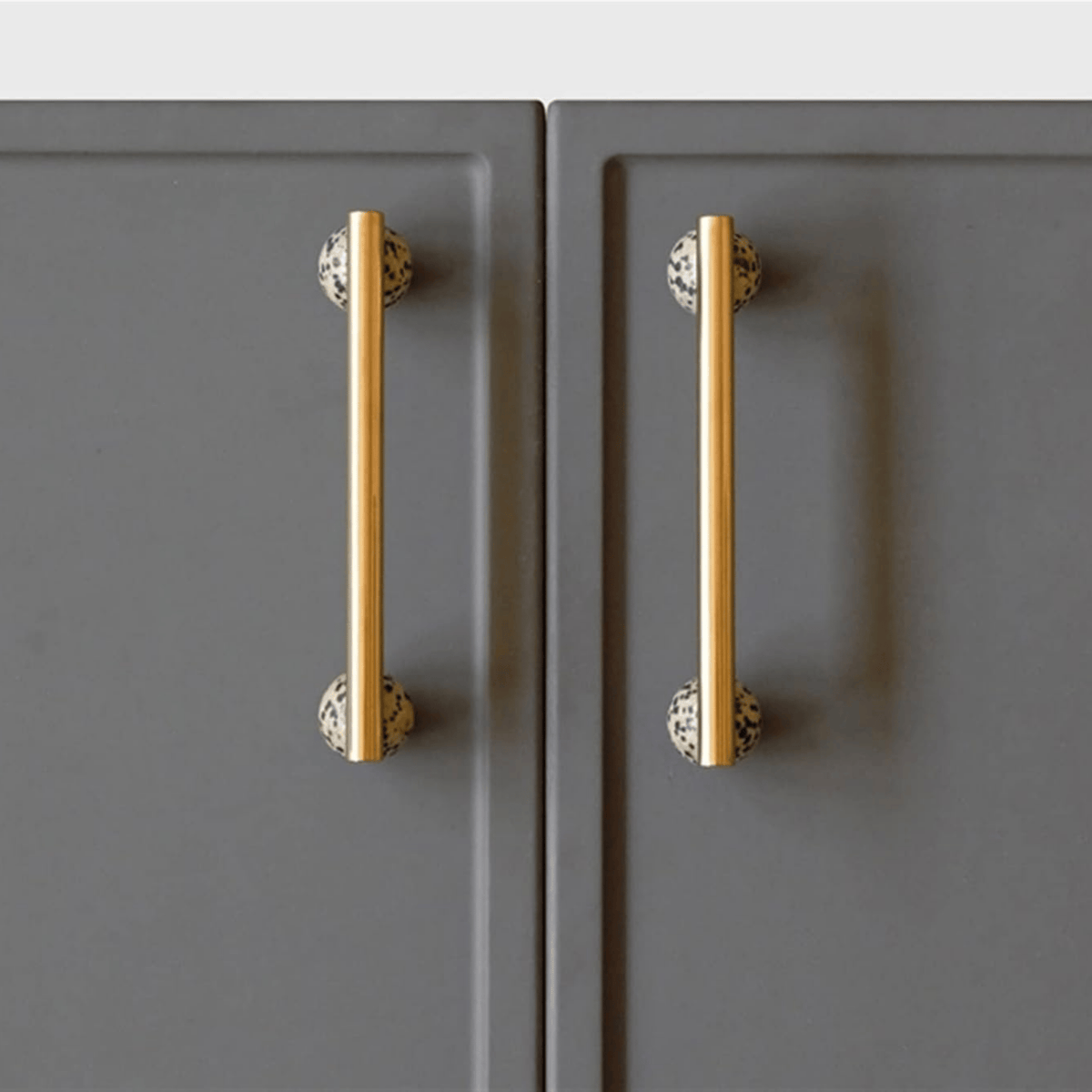 Minimalist brass T-bar cabinet pulls with speckled stone accents on grey shaker doors