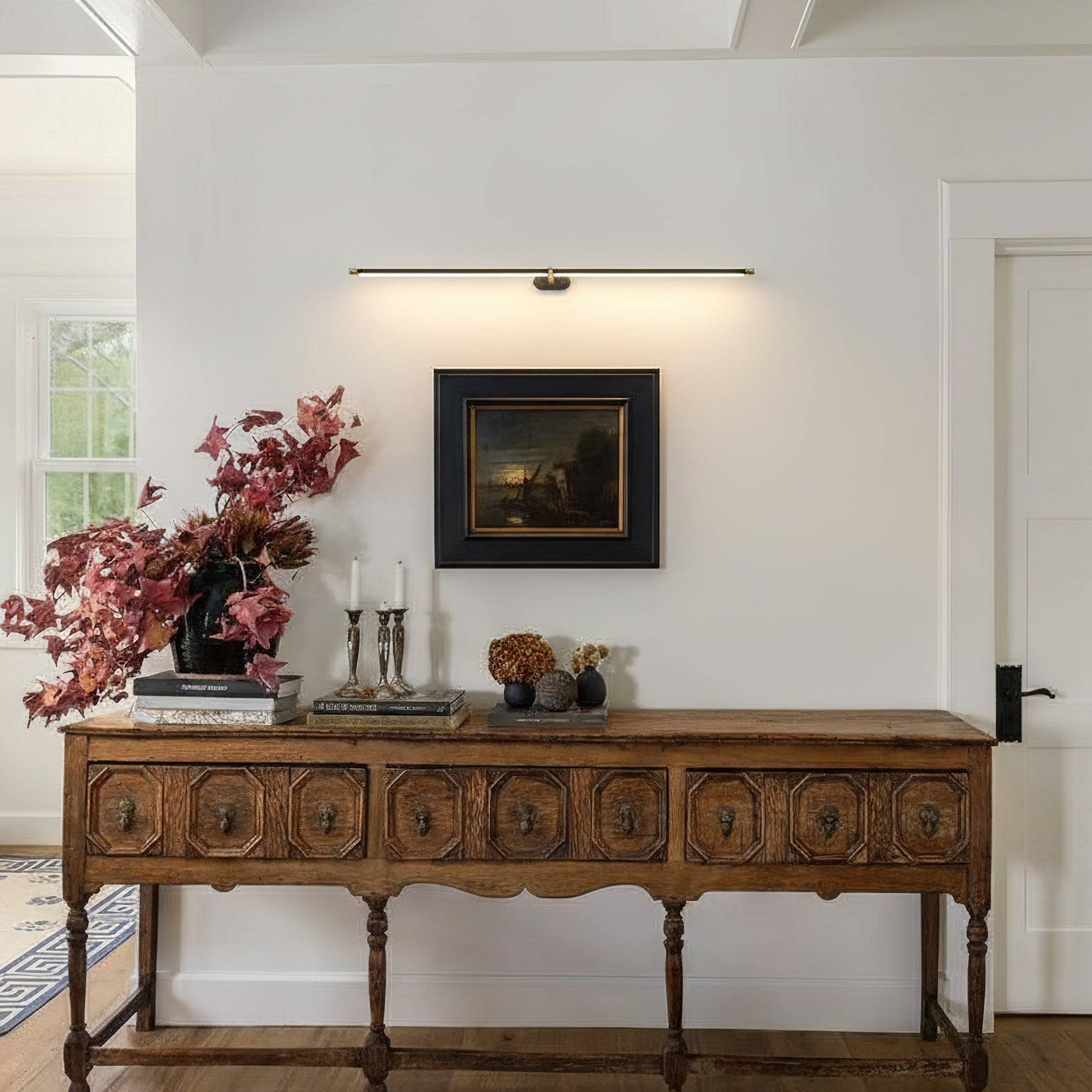 Minimalist black brass linear wall sconce illuminating artwork above console table