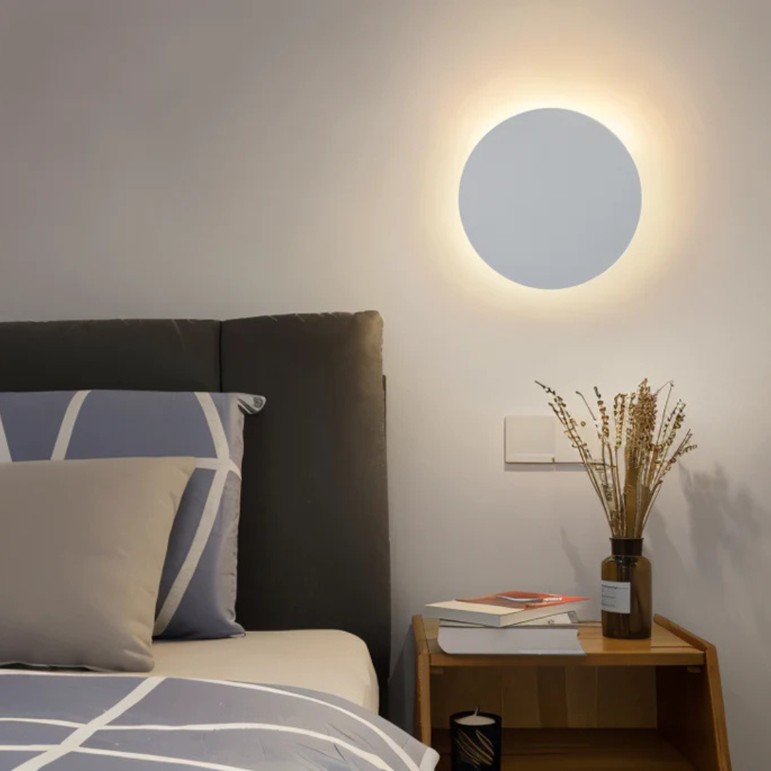 Light blue matte disc wall light above wooden nightstand in bedroom