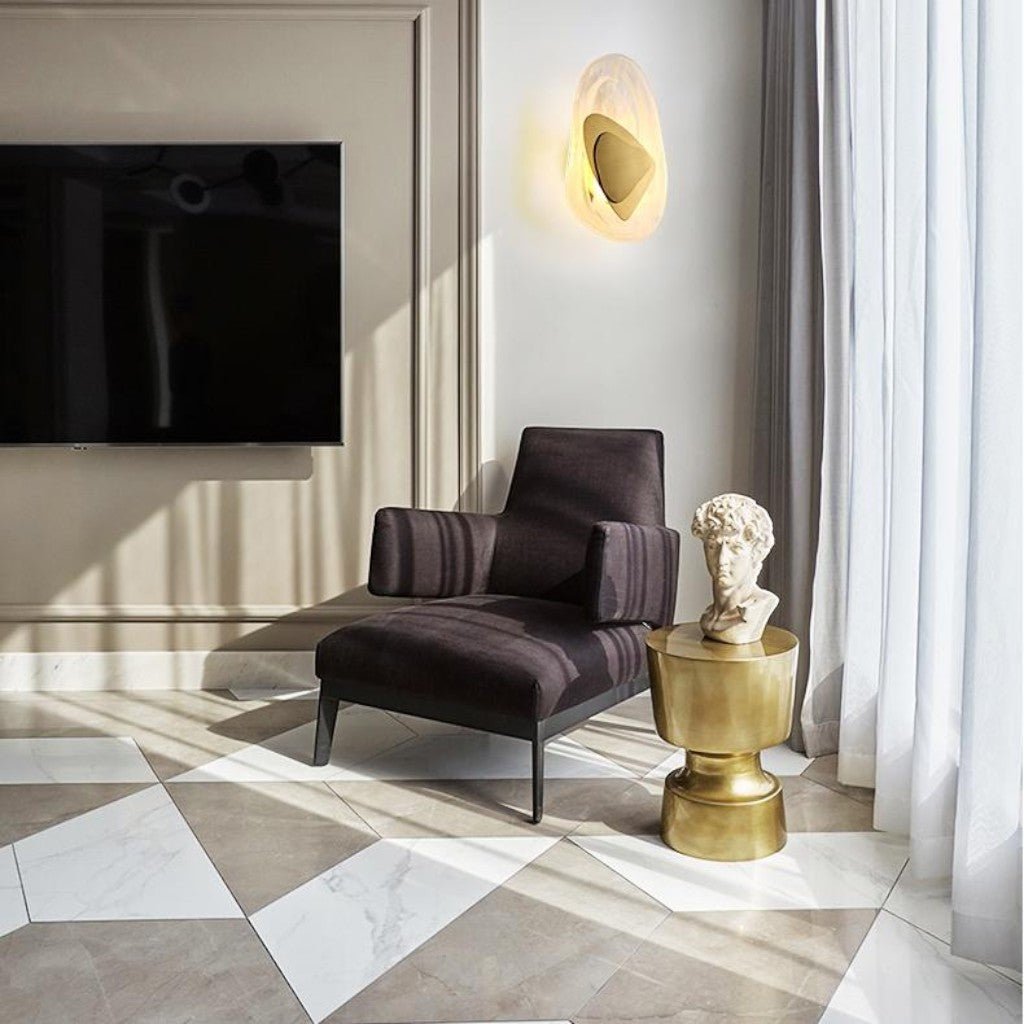 Organic glass wall sconce with gold insert above armchair in living room