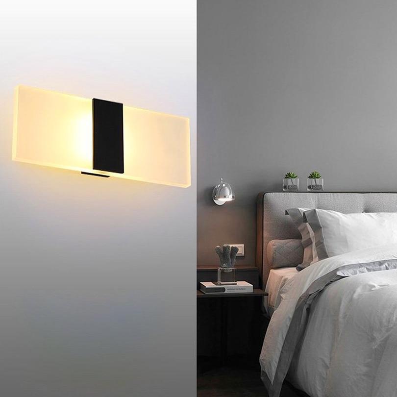 Black acrylic wall sconce mounted in modern bedroom beside upholstered headboard