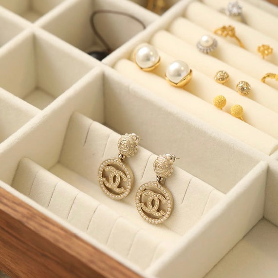 Cream velvet earring slots in walnut jewelry box displaying gold CC logo earrings and pearl studs