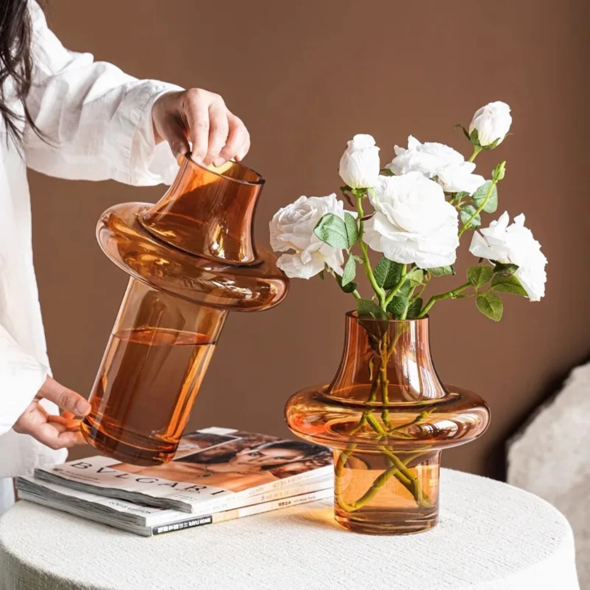 Tall and short amber glass vases with water and roses on magazine stack