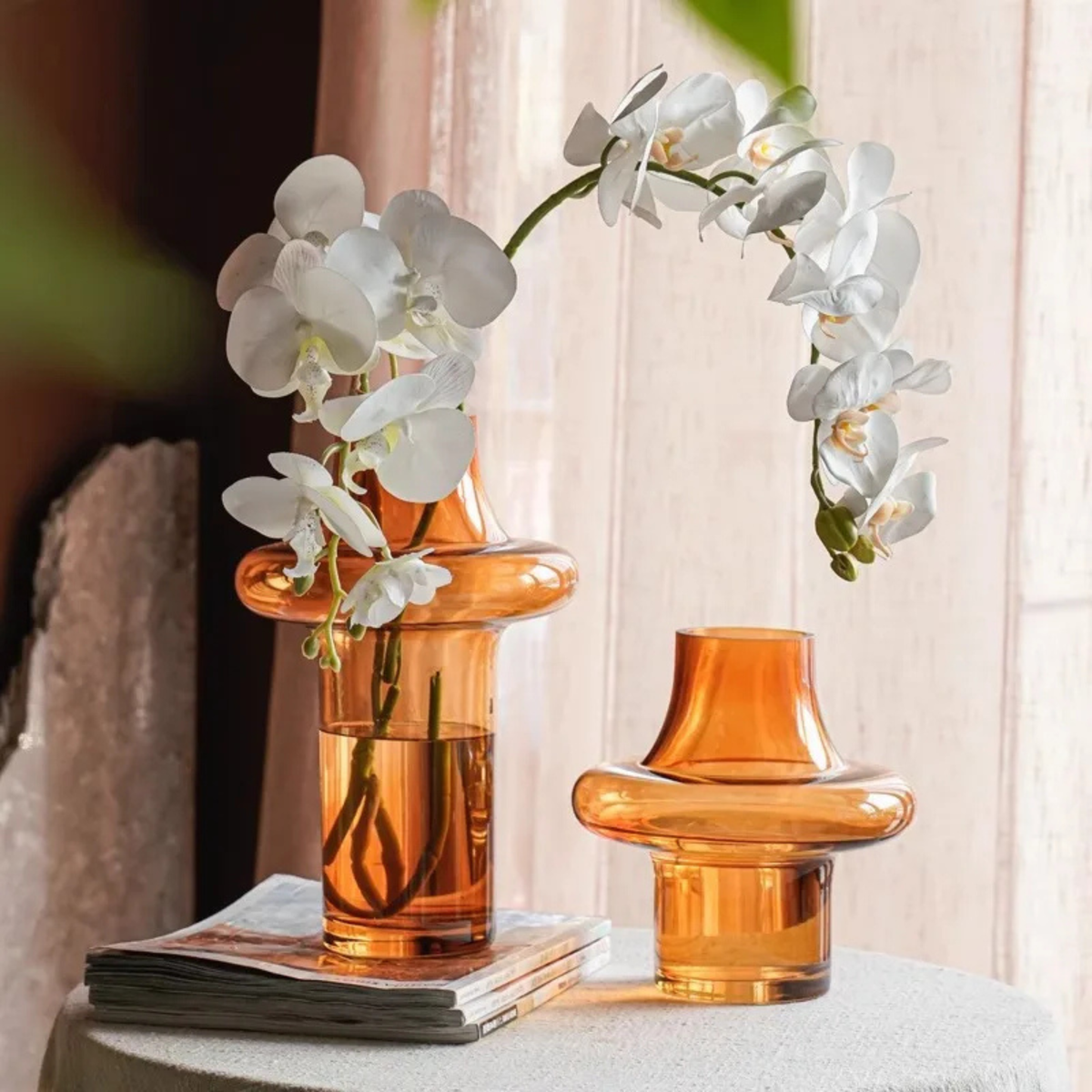 Amber glass flower vase with white orchid stems on textured table
