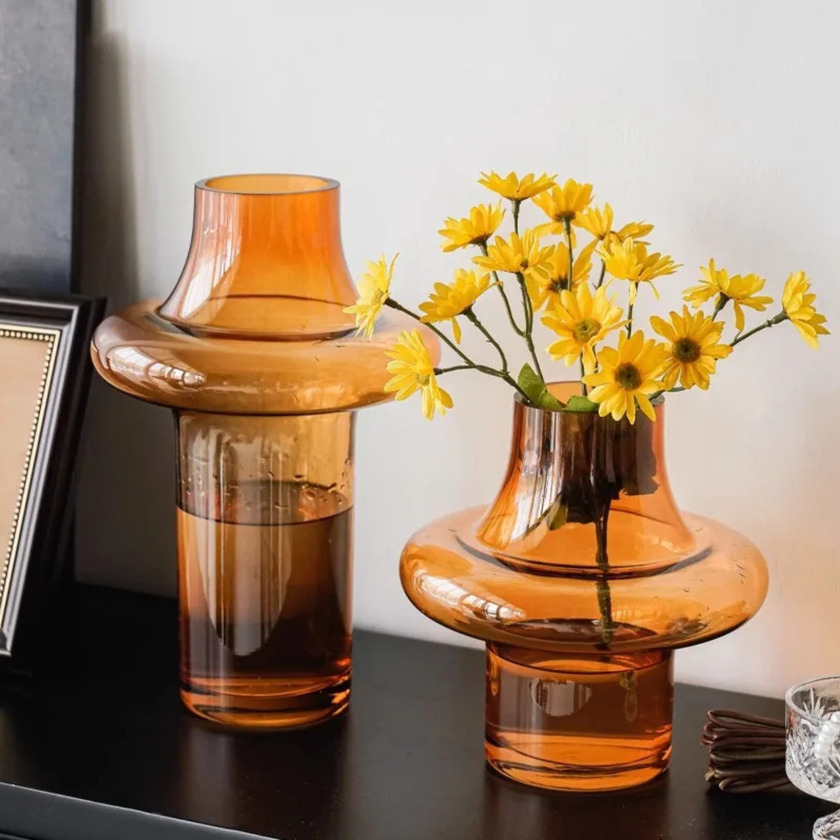 Amber glass planter holding yellow daisies on black tabletop