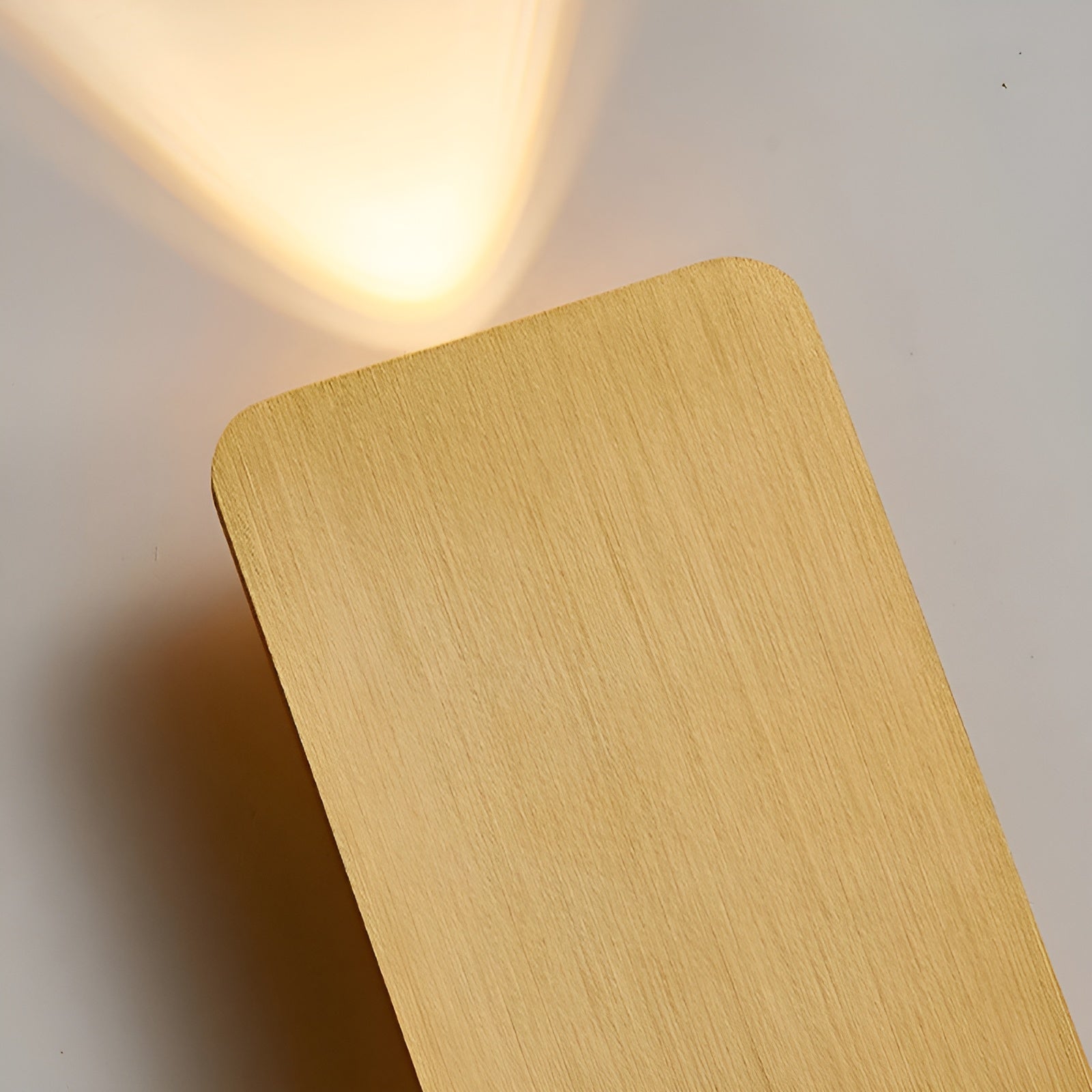 Close-up of gold-toned rectangular wall lamp with horizontal brushed finish and warm light