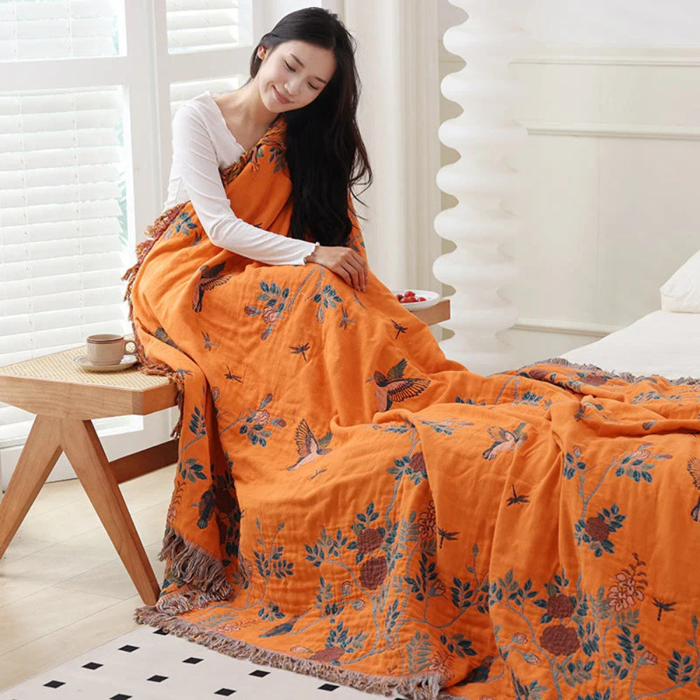 Woman wrapped in orange side of reversible cotton throw blanket with bird embroidery