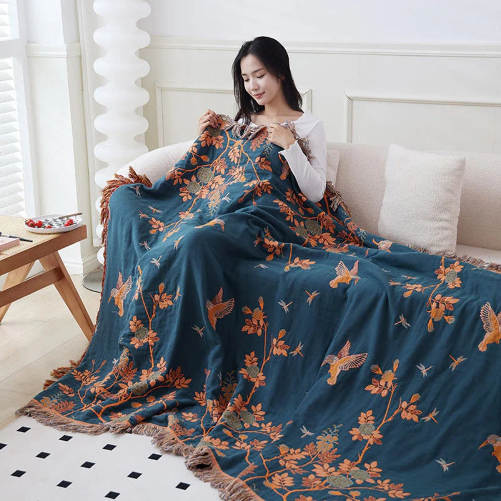 Dark teal woven cotton throw blanket with orange botanical embroidery draped on sofa