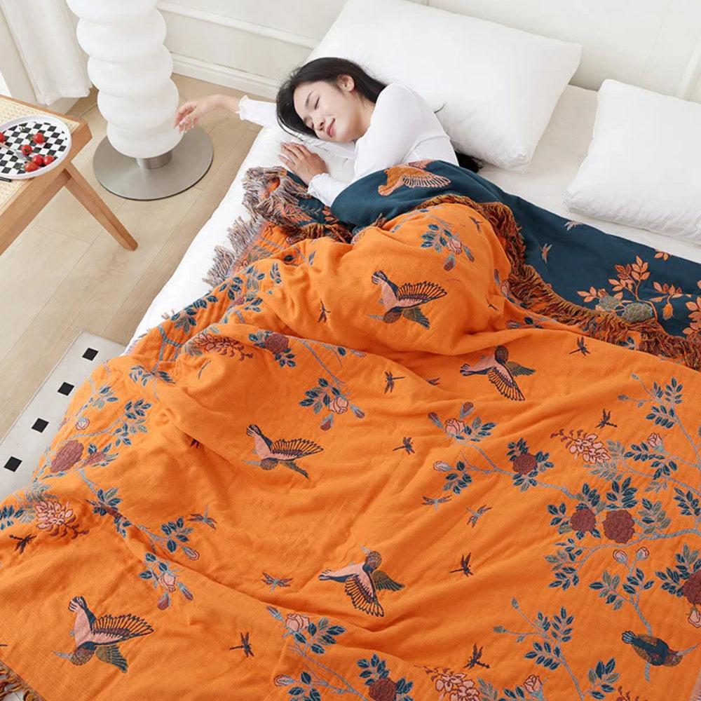 Orange reversible cotton throw blanket with embroidered birds and floral branches on bed