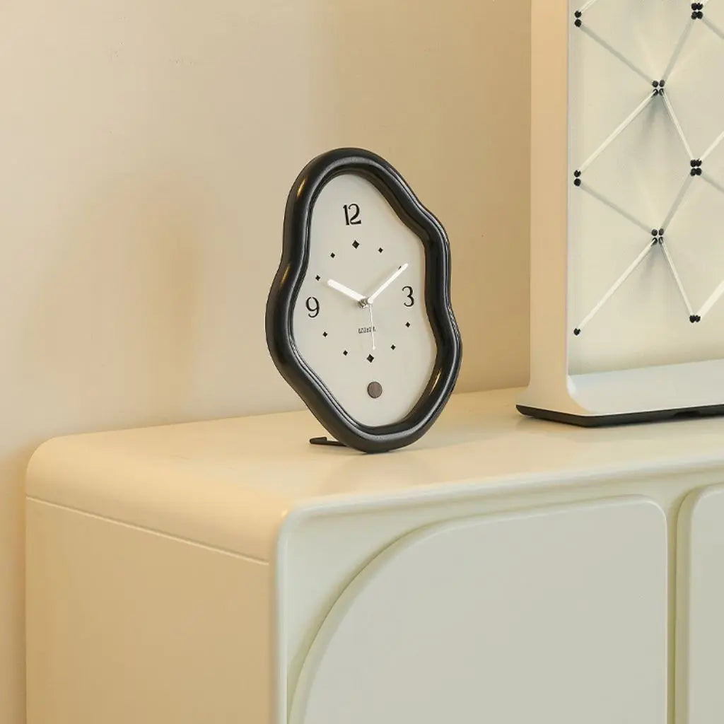Black asymmetrical wooden wall clock on beige cabinet with brand label