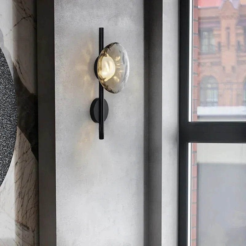 Maintained House Nordic Rippled Glass Wall Sconce - Single Disc on Rod in Smoke Gray Glass / Black on a concrete wall by a window