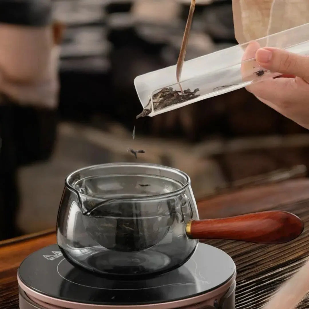 Adding loose leaf tea to smoked gray rotating glass teapot on heater