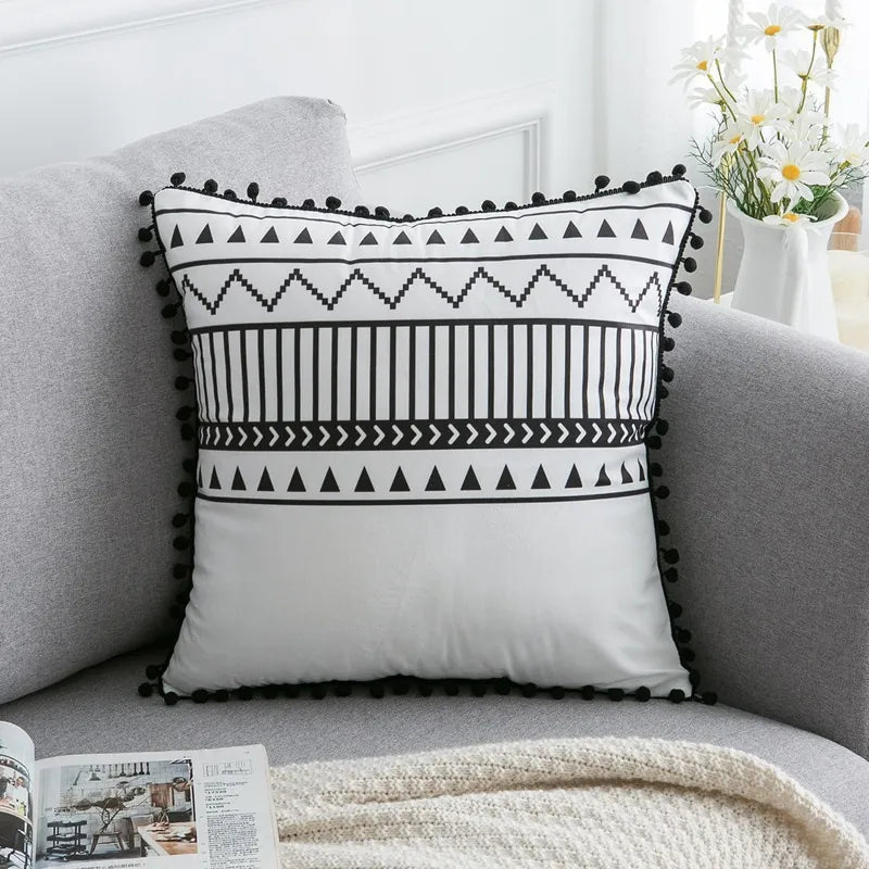 Black and white tribal geometric throw pillow with pom-pom trim on gray sofa