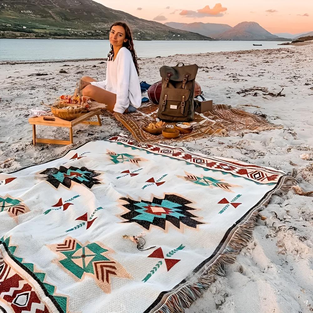 Woman using vibrant tribal pattern beach blanket as outdoor picnic mat at sunset