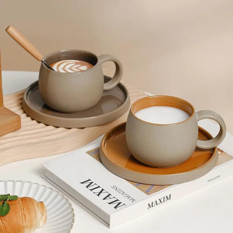 Matte beige ceramic latte cups and saucers with tan-orange interiors on magazine stack