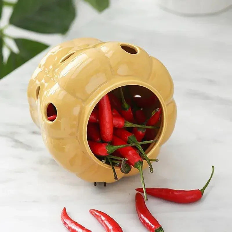 Mustard yellow ceramic garlic storage jar with ventilation holes spilling chilies