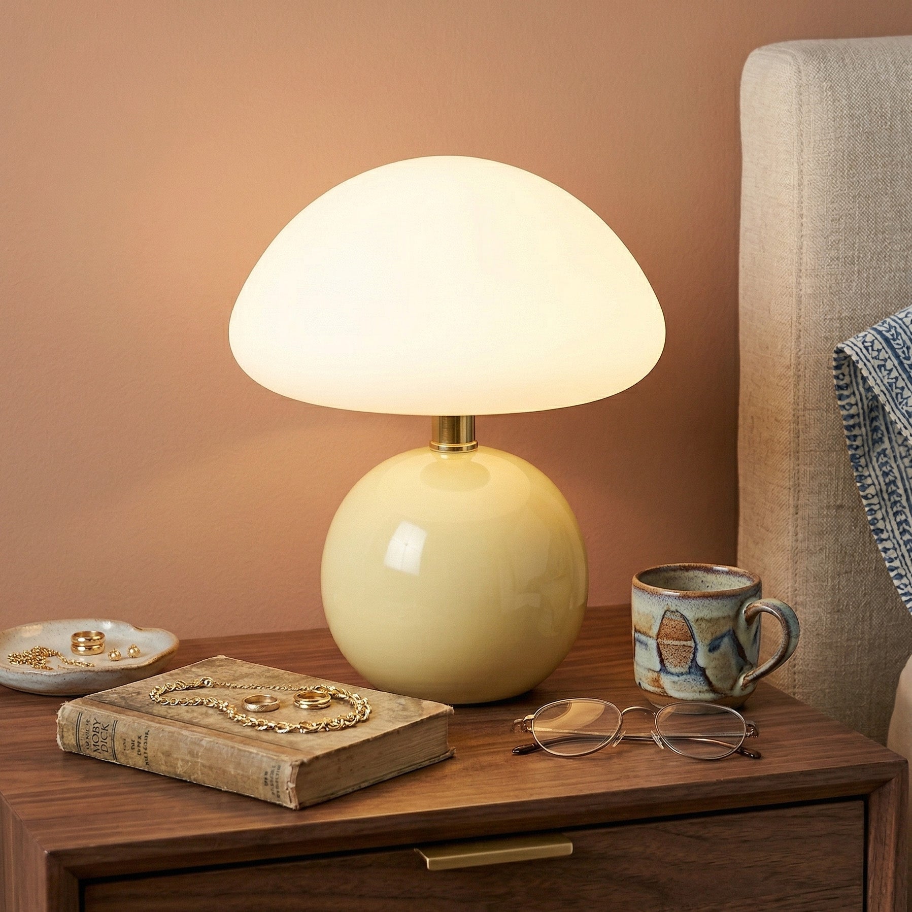 Yellow lamp illuminated on wooden nightstand with book and mug