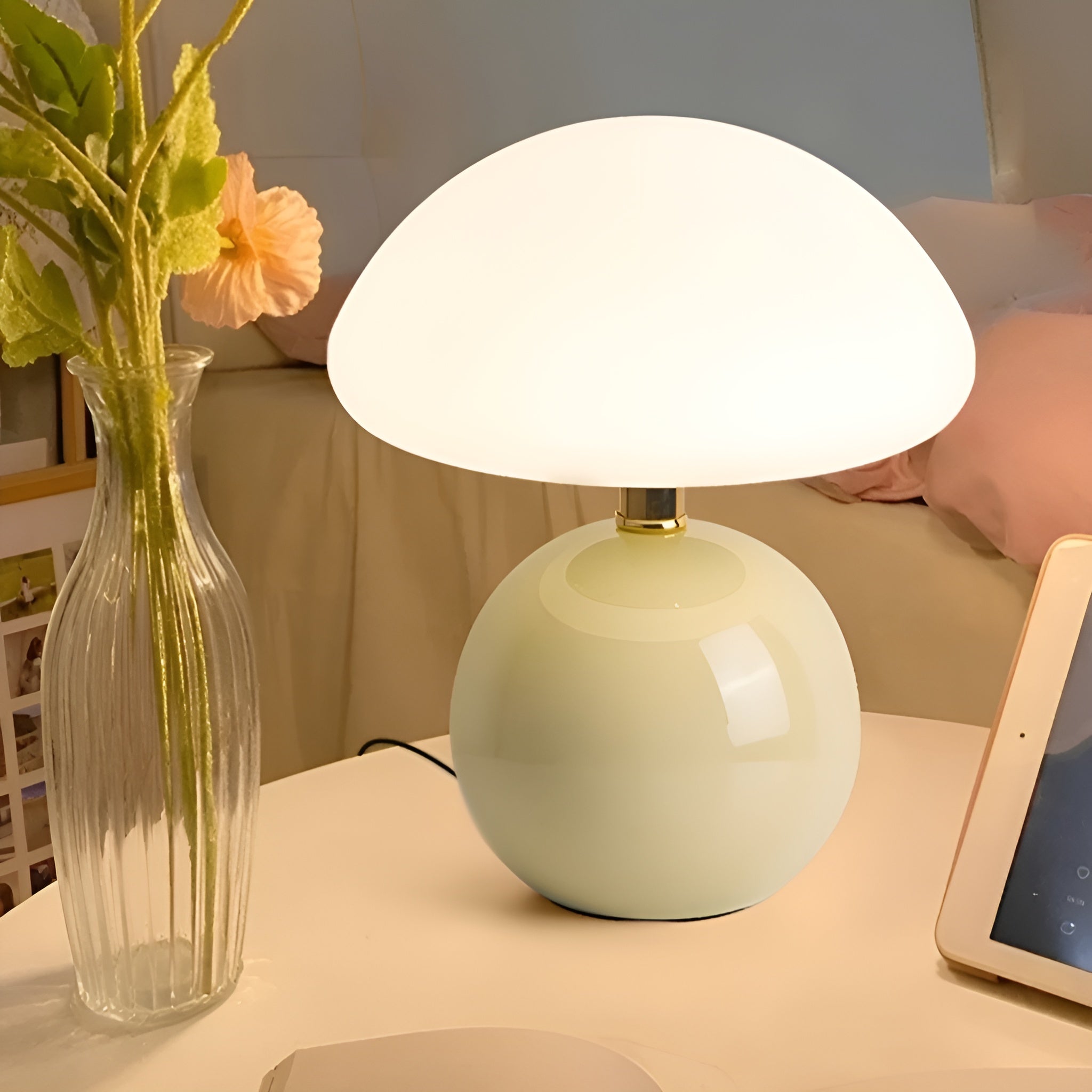 Pale yellow lamp lit in bedroom setting beside tablet and flowers