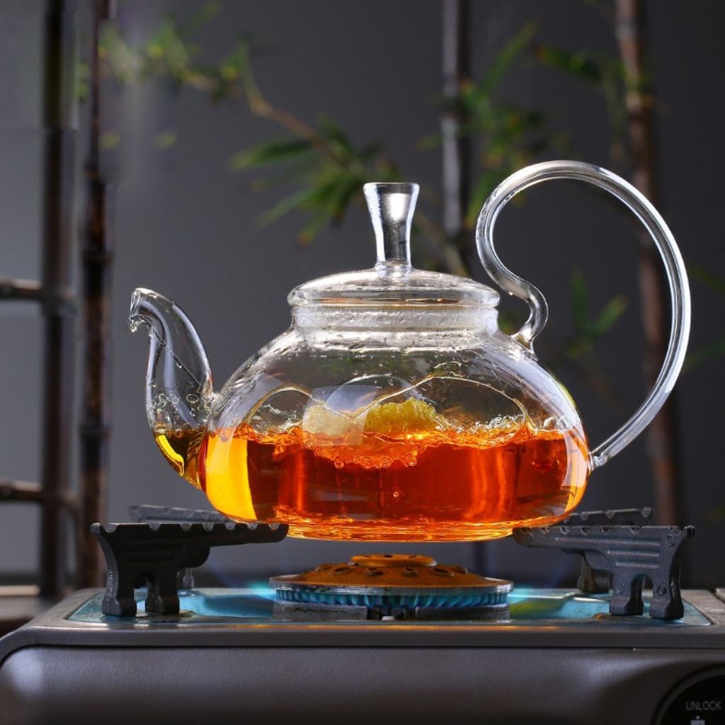 Glass teapot on portable burner brewing floral infuser with bamboo background