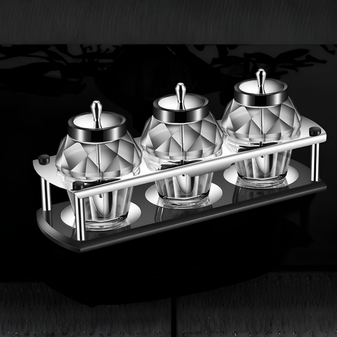 Monochrome view of three diamond-cut glass spice containers with stainless steel lids on modern rack