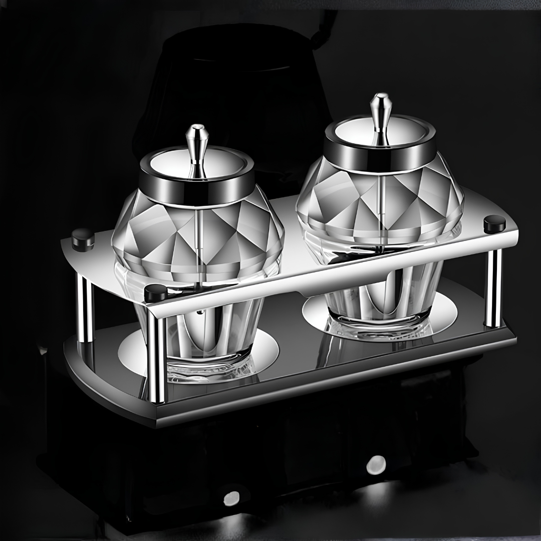 Two diamond-faceted glass seasoning jars with stainless steel lids on curved metal rack against dark background