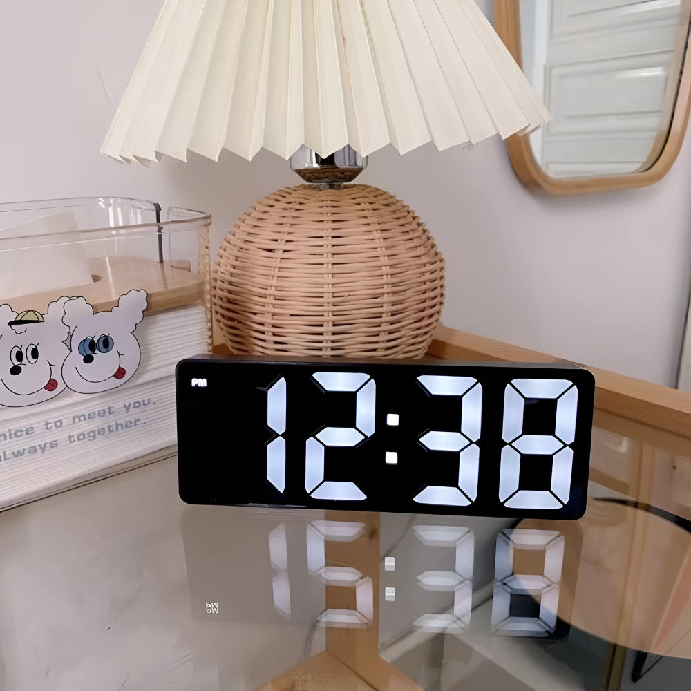 Modern black LED mirror clock showing PM time on glass bedside table