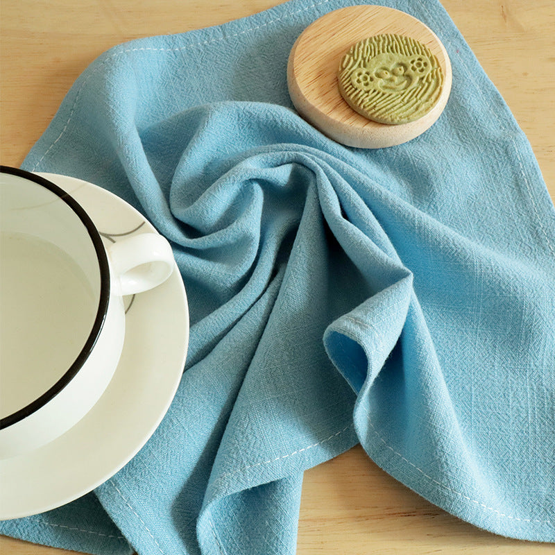 Light blue cotton linen napkin with white stitching beside ceramic cup
