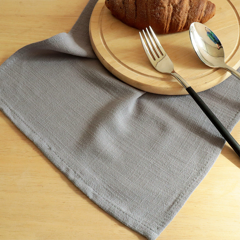 Gray textured cloth napkin under wooden board with croissant and utensils