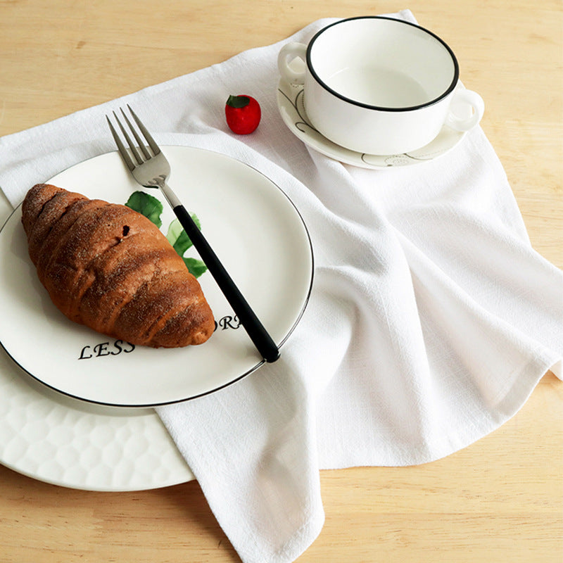 White cotton linen napkin under plate with black rim holding croissant