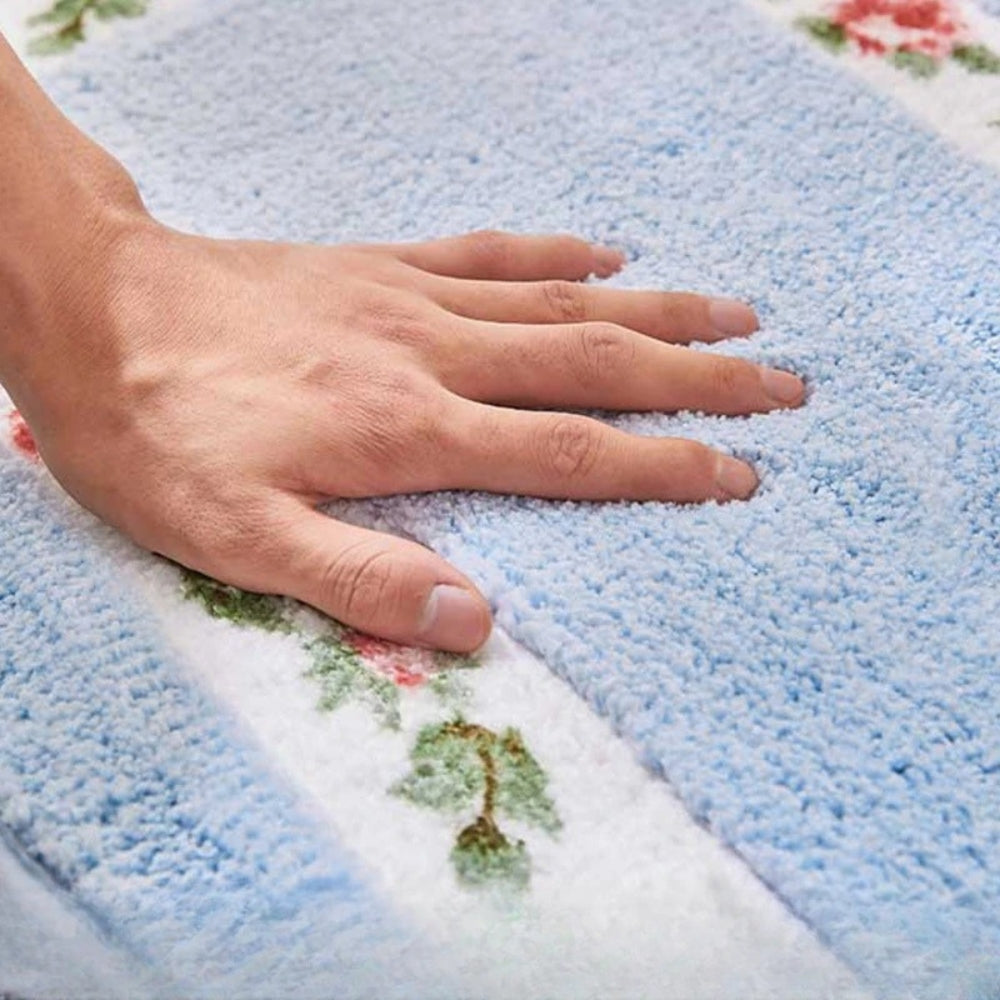 Hand pressing into dense light blue microfiber pile of oval floral bath mat
