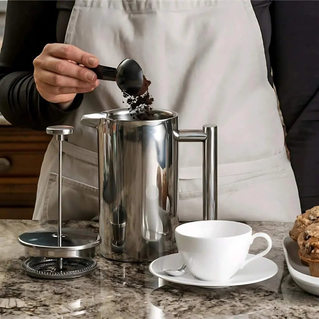Adding ground coffee to stainless steel French press with measuring spoon