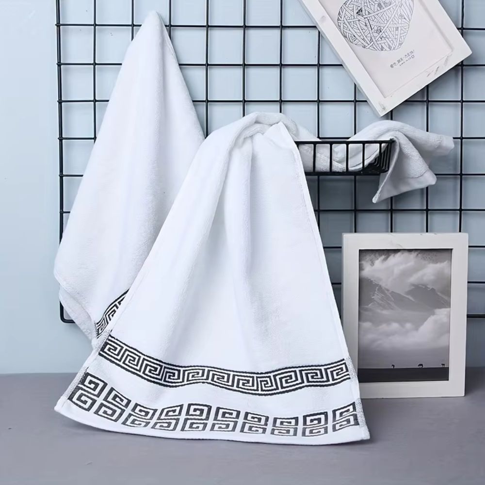 White bath towel with black Greek key border draped on wire shelf