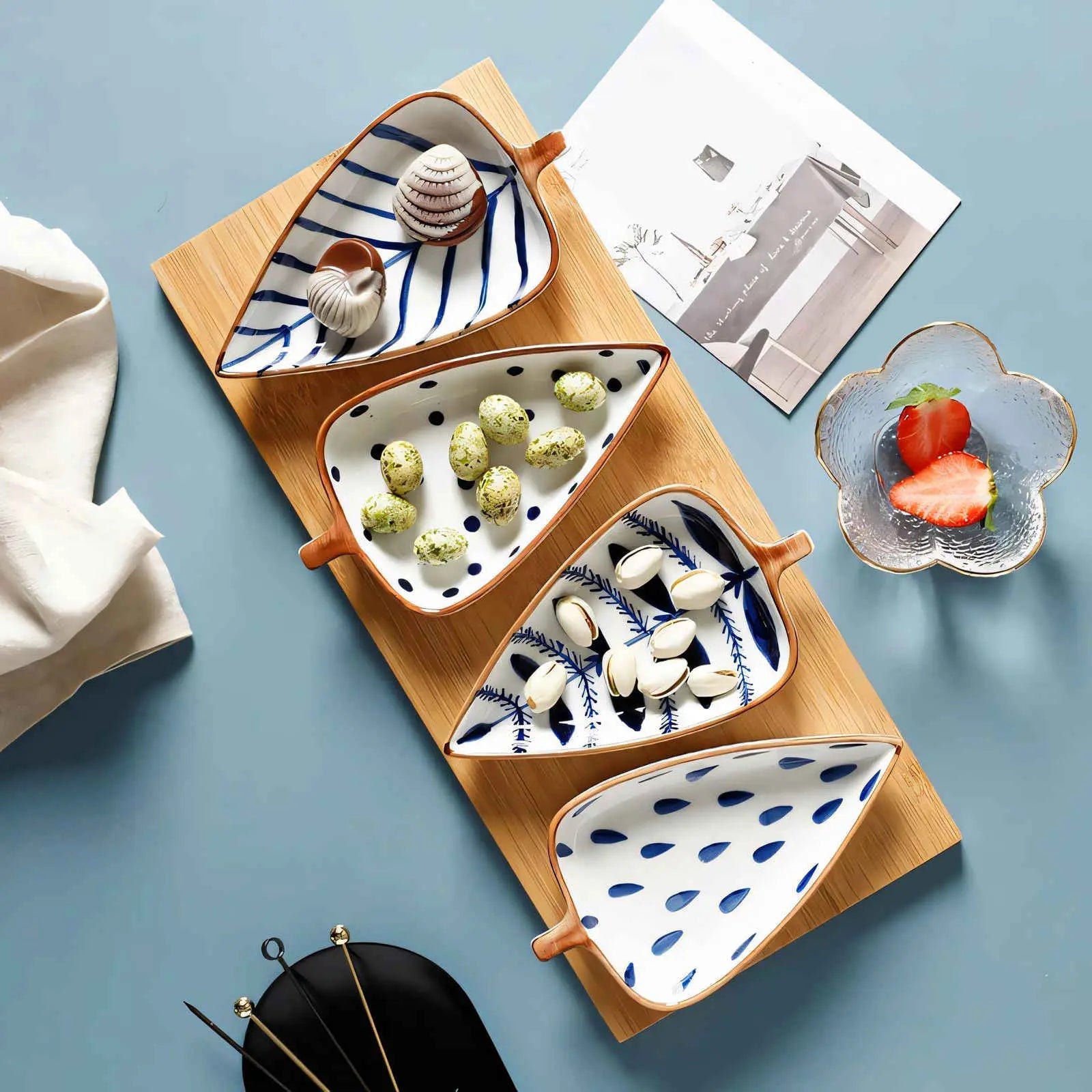 Leaf shaped ceramic snack plates with blue designs holding nuts and chocolate treats