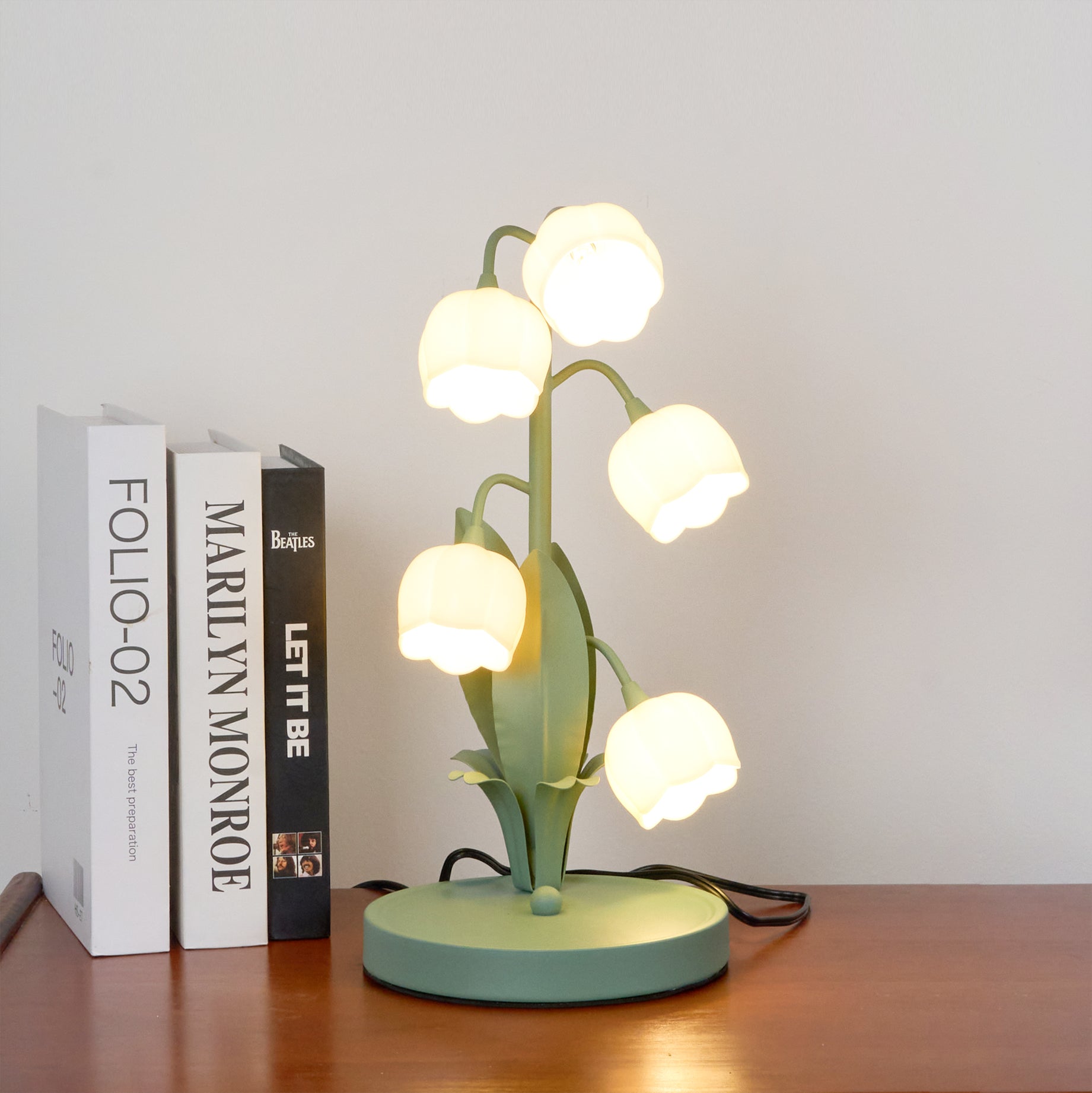 Lit whimsical flower shade lamp emitting soft light beside books on wooden surface