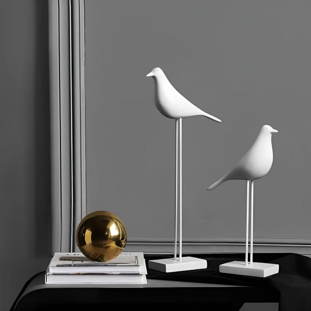 Two white minimalist bird figurines angled together near gold sphere decor